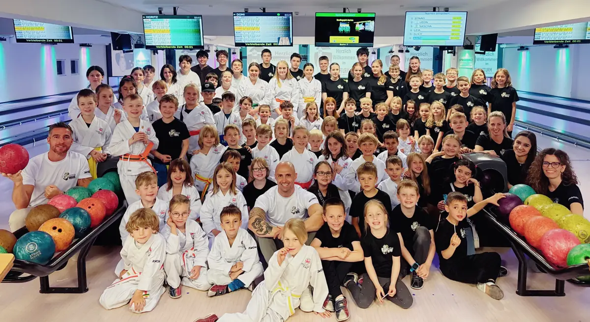Großes Gruppenfoto von Kindern und Jugendlichen in Karateanzügen und Team-Shirts auf der Bowlingbahn