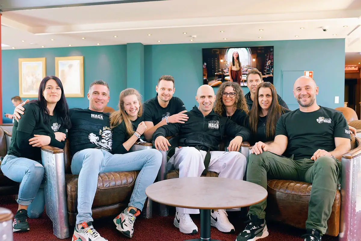 Trainerinnen und Trainer in Team-Shirts auf Ledersofas in einer Lounge