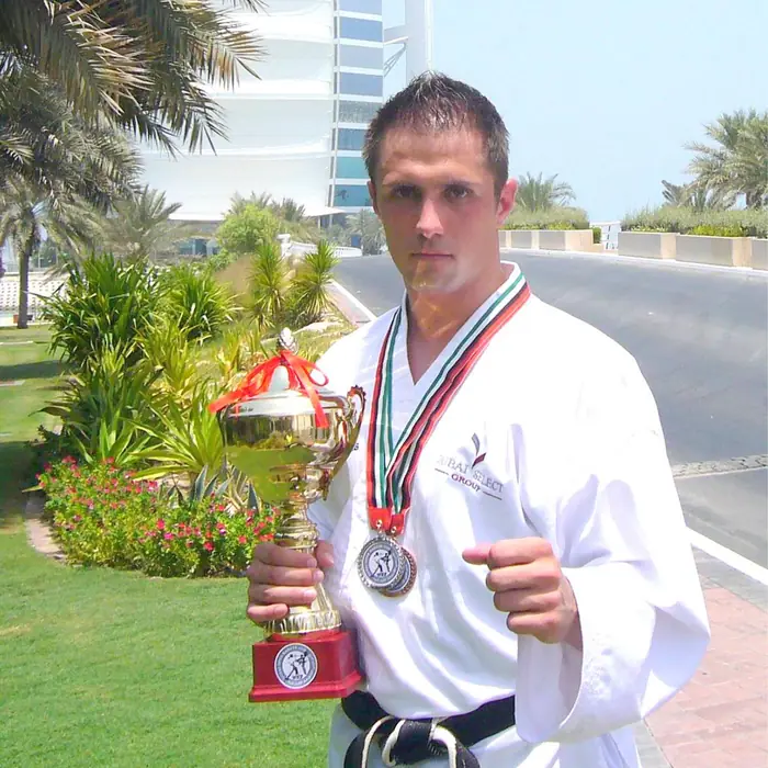 Thomas Lamm im Karateanzug mit Pokal und Medaille unter Palmen