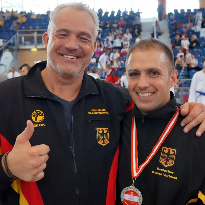 Thomas Lamm mit Medaille neben einem Mann in Deutschland-Jacke