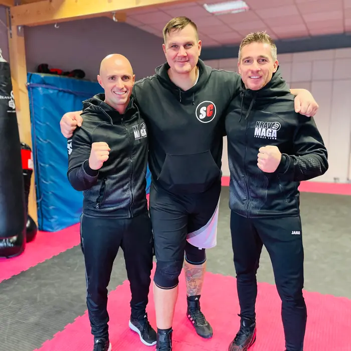 Thomas Lamm mit zwei Männern in dunklen Kapuzenpullovern auf einer pinkfarbenen Trainingsmatte
