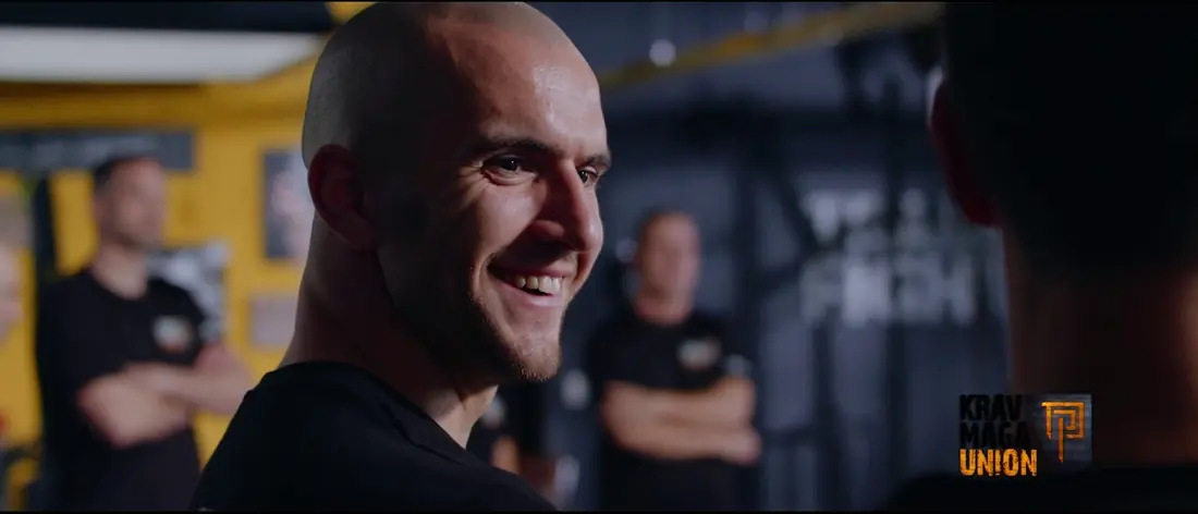 Vorschaubild des Videos: ein lächelnder Trainer in einer Trainingshalle, unten rechts das Logo der Krav Maga Union